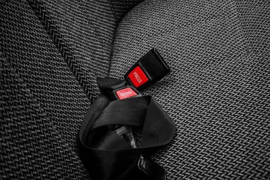A fastened black seatbelt tongue and buckle receiver resting on a woven grey vehicle seat.